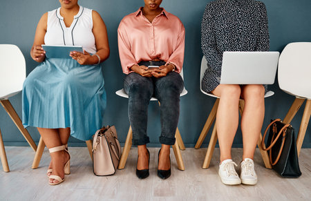 Everyone loves free wifi. Studio shot of a group of unrecognizable businesswomen using wireless technology while sitting in line against a grey background.の写真素材