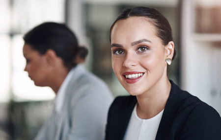 Happy days at the office. Portrait of an attractive young businesswoman posing inside an office with her colleague in the background.の写真素材