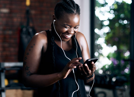 Adding a few new tracks to her workout. an attractive young female athlete listening to music while standing in the gym.の写真素材