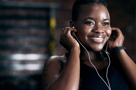Music puts her in the zone. an attractive young female athlete listening to music while standing in the gym.の写真素材