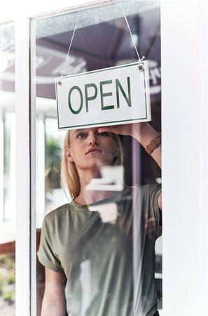 Were open for business. an attractive young hairdresser hanging up an open sign on the window of her...