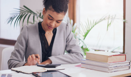 Shes money-minded. an attractive young businesswoman using a calculator and a notebook while working on her finances in her office.の写真素材