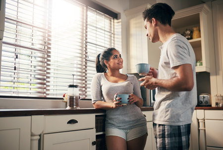 Coffee is a conversation starter. a young couple having coffee in their kitchen at home.の写真素材