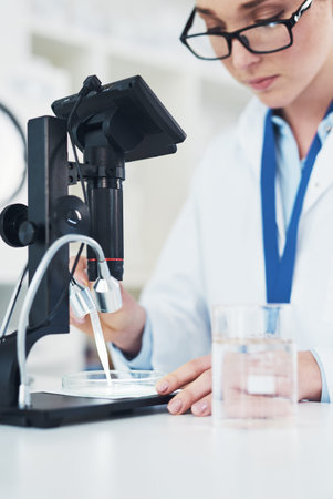 Just a little bit for starters. a focused young female scientist looking through a microscope while...