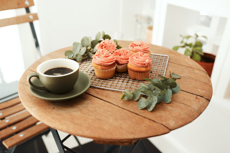 Coffee and cupcakes are the best remedies for anything. freshly baked cupcakes on a metal tray and a cup of coffee on a table indoors.の写真素材
