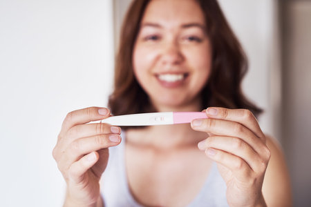 I have some good news to share. a young woman holding up a pregnancy test at home.の写真素材
