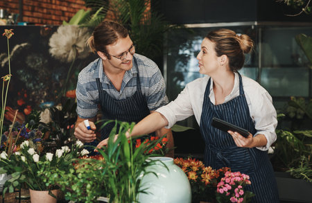 Were both specialists in this field. two young florists watering flowers and working together inside their plant nursery.の写真素材