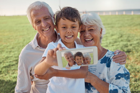 Phone, selfie and happy grandparents with child outdoor in nature on family picnic together. Happiness, smile and elderly man and woman in retirement taking picture on smartphone with boy grandchild.の写真素材