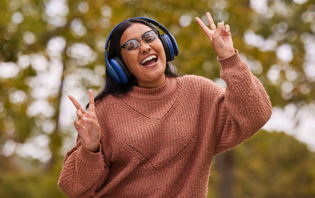 Music, headphones and peace hand sign of a woman from India in nature on a walk or hike. Portrait of...