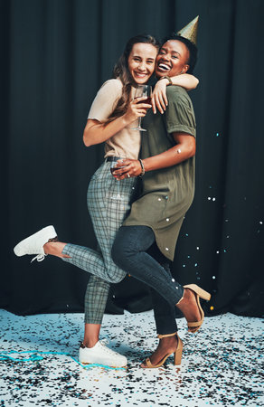With friends like these, who needs anything else. Full length portrait of two attractive young women standing and hugging each other during a New Years party.の写真素材