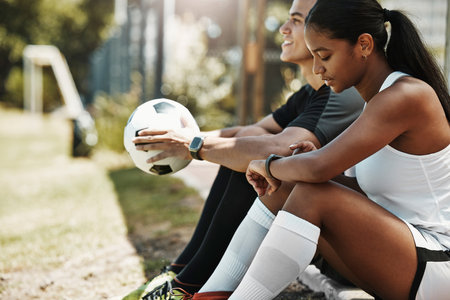 Fitness, smartwatch and soccer couple check time, pulse and heart rate with technology after exercise, training or practice. Man, woman or rest with football, cardio or sport workout outdoor on fieldの写真素材