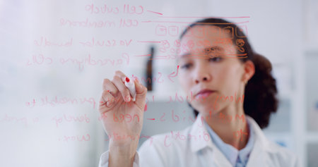 Figuring out how different scientific systems work. a young scientist writing notes on a glass wall in a lab.の写真素材