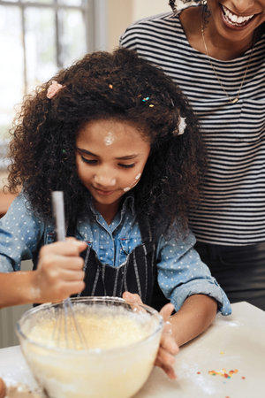 Its getting messy in the kitchen. a little girl baking at home with her mothers help.