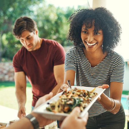 Good food always brings everyone together. a beautiful young woman passing over a plate of food at a...