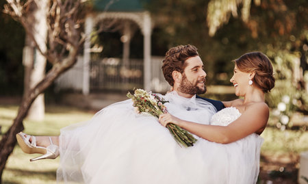 The love of his life in his hands. an affectionate young groom carrying his bride while standing outdoors on their wedding day.の写真素材