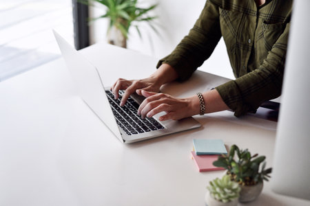 Updating all the work files on the system. an unrecognizable businesswoman typing on her laptop while sitting alone at her desk in the office.の写真素材