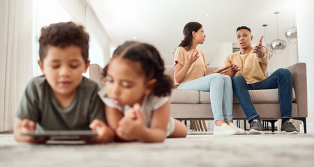 Mother, father and disagreement on living room sofa while children are playing with tablet on the floor at home. Mama and dad fighting, argue or conflict in difficult situation on couch in disputeの写真素材