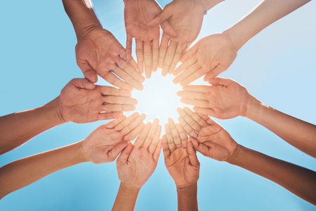 Hands in circle together, blue sky and sun, diversity and community in collaboration for support and success. Teamwork, hands together and summer sunshine, positive vision and trust between friends.の写真素材