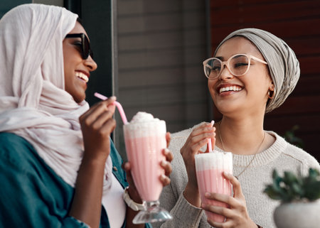 You know Id never say no to milkshakes. two affectionate young girlfriends having milkshakes together in a cafe while dressed in hijab.の写真素材