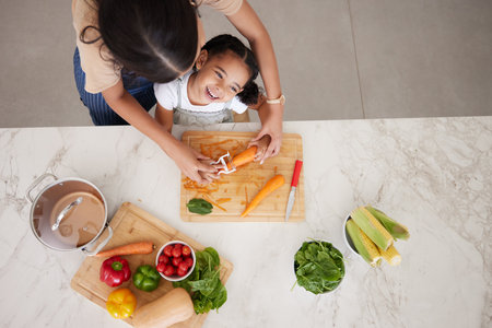 Development, child and mother in kitchen, vegetables and learn cooking together being happy, smile and safety. Top view, mama and girl peeling food, childcare and cutting veggies and organic dinner.の写真素材