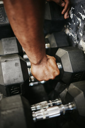 Dumbbell, man hands and weight training in gym, fitness club or exercise studio for healthy lifestyle, wellness and strong muscle. Bodybuilder, personal trainer or coach workout power with heavy ironの写真素材