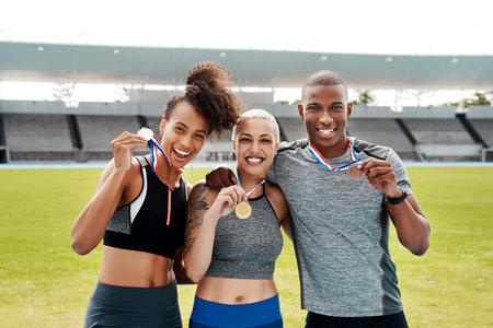 We are champions. Cropped portrait of a diverse group of athletes standing together and holding up medals after winning a running race.の写真素材