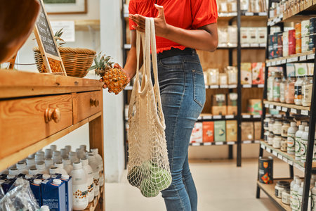 Woman, fruit shopping and pineapple in hand with ripe avo in bag at a supermarket grocery store looking for healthy food at discount price. Healthy, organic and natural fresh groceries for home lunchの写真素材