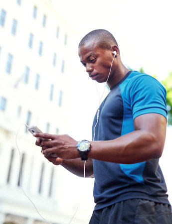 a handsome young man listening to music and using his cellphone while exercising outdoors in the city.の写真素材