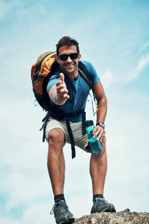 Take my hand. Portrait of a cheerful young man stretching out his hand to help while going for a...