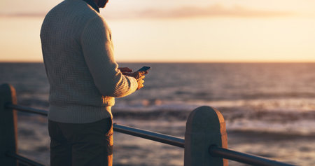 Ill be coming home a little bit late tonight. Rearview shot of a man using his cellphone at the beach.の写真素材