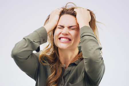 Studio shot of an attractive young woman looking stressed out against a grey background.