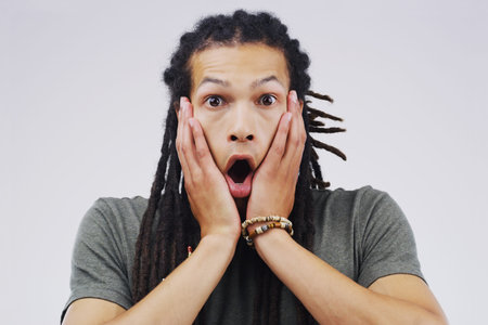 Studio portrait of a handsome young man looking shocked against a grey background.