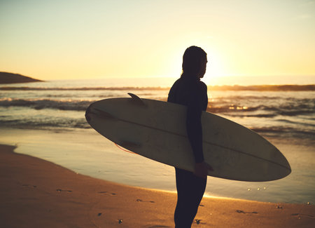 Waiting for the perfect waves to come crashing in. Rearview shot of a young man carrying a surfboard...