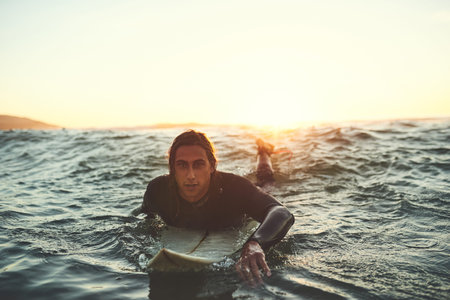 Lifes better when youre surfing. a young man paddling on a surfboard in the sea.