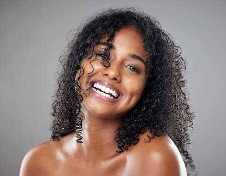 Black woman, beauty and hair in face, makeup or smile against studio background with happiness. Model, hair care and happy with cosmetics for skincare, self care or portrait with glow, skin or curlyの写真素材