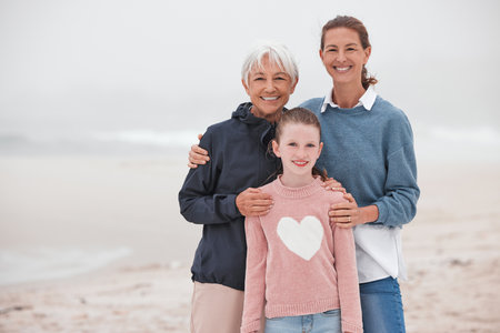 Mother, grandma and child at beach in portrait, bonding or love in winter, mist or cloud by sea. Mom, girl and senior for smile, happy or care in family, happiness or together at ocean on vacationの写真素材