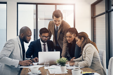 They dont stop until the strategy is perfect. a group of young businesspeople using a laptop together during a meeting in a modern office.の写真素材