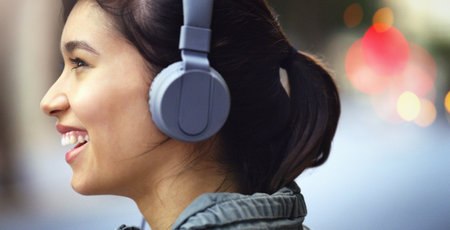 Blocking out the city noise. Closeup shot of a cheerful young woman listening to music on her headphones while walking through the city.の写真素材