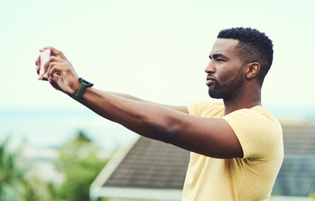 Getting a few pictures of myself on holiday. a handsome young man taking a selfie with his cellphone while relaxing outdoors on holiday.の写真素材