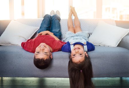 I guess things are looking up for them. Portrait of two young children lying upside down on a couch at home.の写真素材