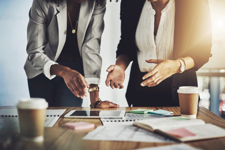 Discovering what the world online has to offer. Closeup shot of two businesswomen using a digital tablet while going through paperwork in an office.の写真素材