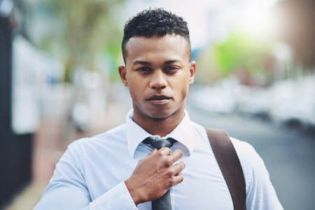 Look the part to respect the part. Portrait of a handsome young businessman adjusting his tie while out in the city.の写真素材