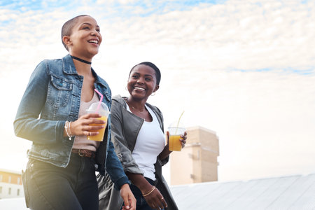 Sometimes happiness is a smile away. Low angle shot of two young women walking in the city laughing while holding their cool drinks.の写真素材