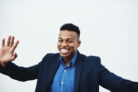 Hi Im the new guy. Studio portrait of a young businessman posing with his arm raised and waving against a grey background.の写真素材