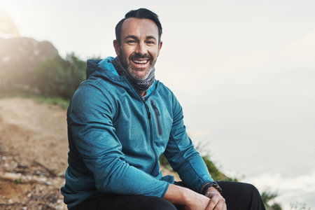 This is what happiness looks like. Portrait of a middle aged male hiker sitting down and smiling in the mountains.の写真素材