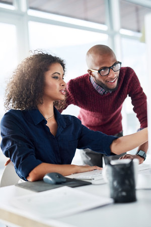 She trusts his advice. a male supervisor helping an attractive young businesswoman while working in their office.の写真素材