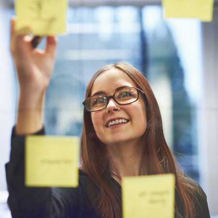 She enjoys coming up with ideas. a young businesswoman brainstorming on a glass wall in an office.の写真素材
