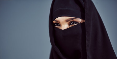 Its in her eyes. Studio shot of a young arabic woman wearing a burka against a gray background.の写真素材