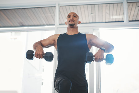 Im stronger than all my fears. a young man working out with dumbbells at the gym.