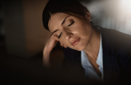 Maybe if I took a power nap at my desk...a young businesswoman falling asleep at her desk during a late night in a modern office.の写真素材